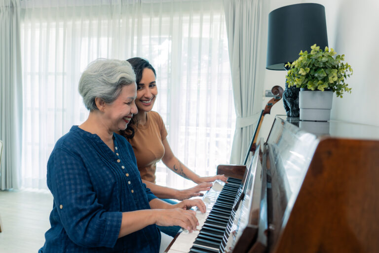 A mixed-race mid-adult daughter joyfully playing piano with her healthy and cheerful Asian senior retired mother on the weekend.